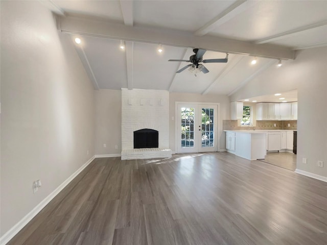 unfurnished living room featuring ceiling fan, french doors, a brick fireplace, vaulted ceiling with beams, and hardwood / wood-style floors