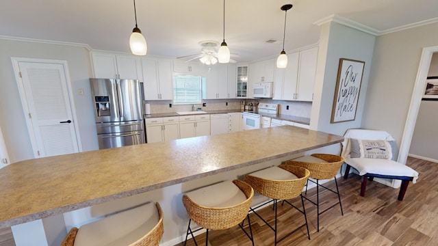 kitchen featuring white cabinetry, sink, crown molding, white appliances, and a breakfast bar area