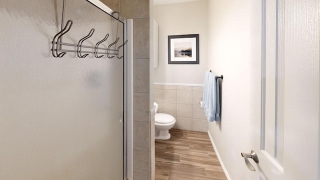 bathroom with walk in shower, toilet, tile walls, and hardwood / wood-style flooring