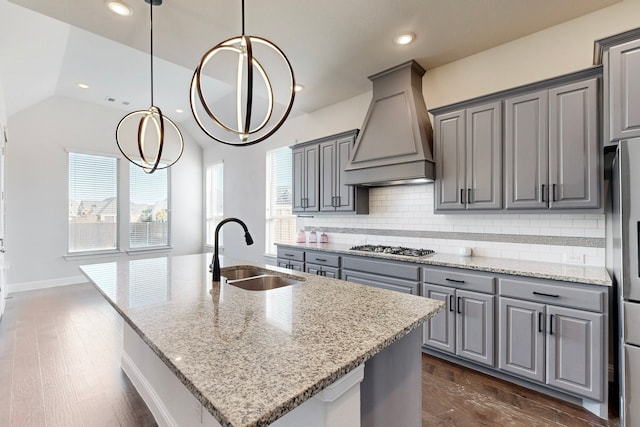 kitchen with custom exhaust hood, a center island with sink, sink, dark hardwood / wood-style floors, and light stone countertops