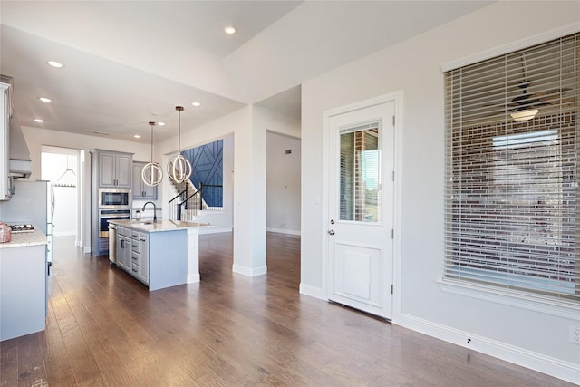 kitchen featuring gray cabinetry, stainless steel appliances, dark wood-type flooring, an island with sink, and pendant lighting