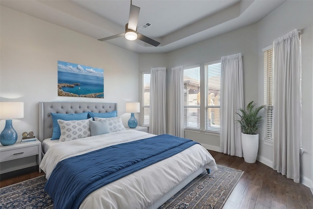 bedroom featuring ceiling fan, dark wood-type flooring, and a tray ceiling