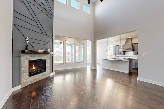 unfurnished living room featuring dark wood-type flooring, a towering ceiling, a healthy amount of sunlight, and a brick fireplace