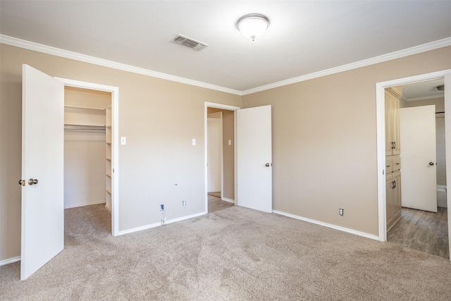 unfurnished bedroom with light colored carpet, a walk in closet, ornamental molding, and ensuite bath