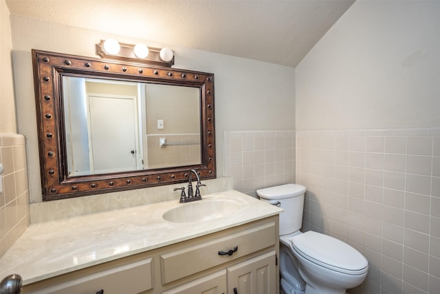 bathroom with a textured ceiling, vanity, toilet, and tile walls