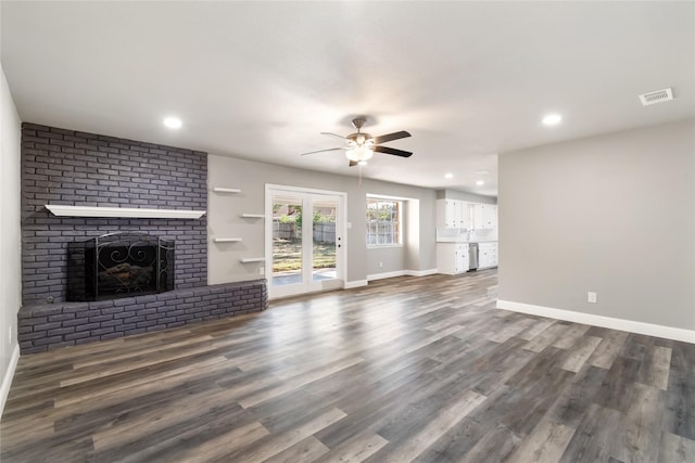 unfurnished living room with ceiling fan, french doors, dark wood-type flooring, and a brick fireplace