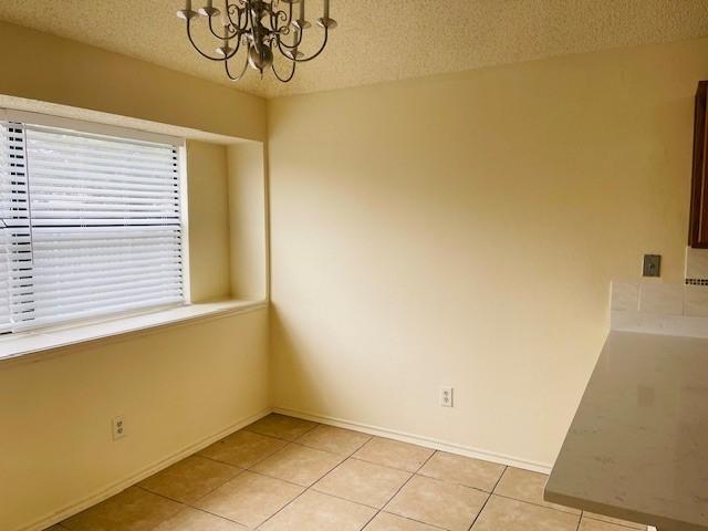 unfurnished dining area with a chandelier, light tile patterned floors, and a textured ceiling