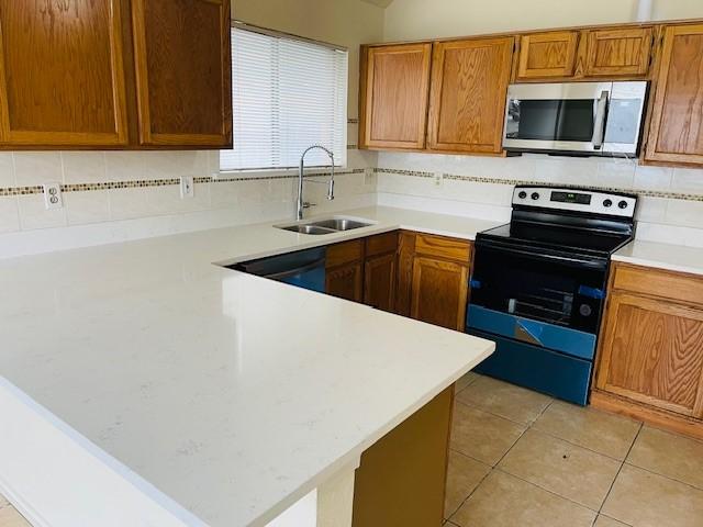 kitchen with light countertops, stainless steel microwave, a sink, and electric range