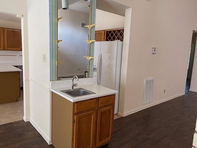 kitchen featuring dark wood-style flooring, light countertops, visible vents, brown cabinetry, and a sink