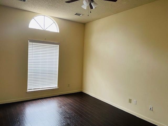 spare room featuring dark wood-style floors, visible vents, baseboards, and a ceiling fan