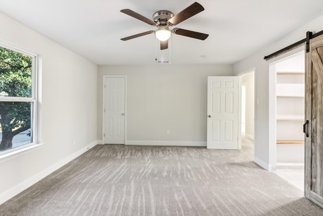 unfurnished room with a barn door, light colored carpet, and ceiling fan