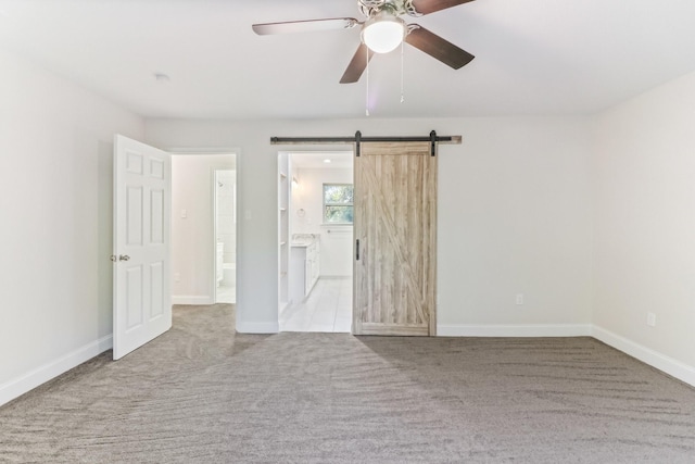 spare room featuring ceiling fan, a barn door, and light carpet