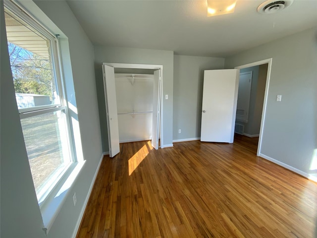 unfurnished bedroom with a closet, wood-type flooring, and multiple windows