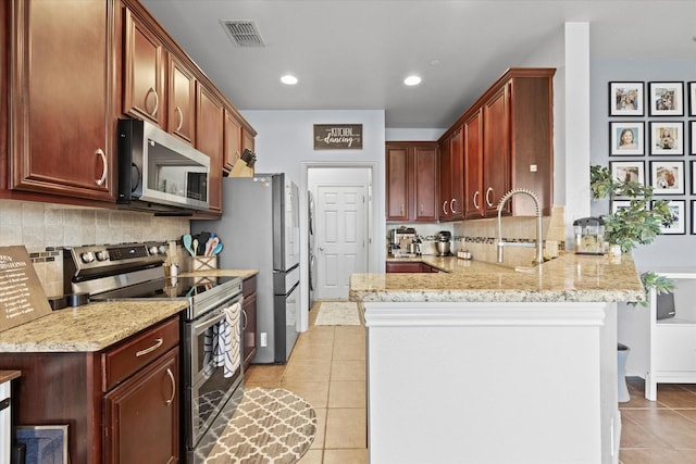 kitchen featuring light tile patterned flooring, light stone countertops, kitchen peninsula, and stainless steel appliances