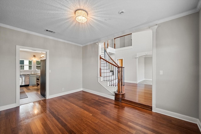 spare room featuring an inviting chandelier, wood-type flooring, ornamental molding, a textured ceiling, and ornate columns