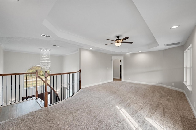 carpeted spare room featuring a raised ceiling and ceiling fan with notable chandelier