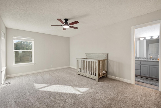 unfurnished bedroom with sink, a crib, ceiling fan, a textured ceiling, and light carpet