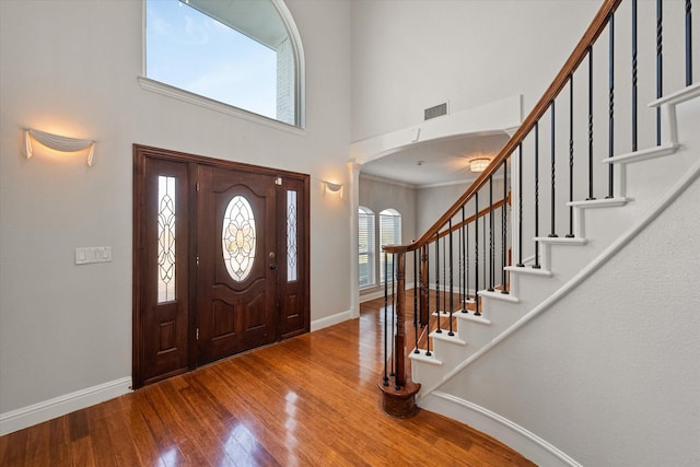 foyer entrance with a high ceiling, wood-type flooring, and ornamental molding