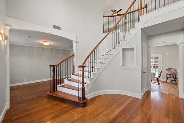 stairway with ornate columns, crown molding, a towering ceiling, ceiling fan, and hardwood / wood-style floors