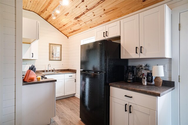 kitchen with sink, white cabinets, wood ceiling, black fridge, and light wood-type flooring