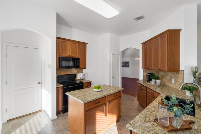 kitchen featuring light tile patterned floors, tasteful backsplash, light stone counters, a kitchen island, and black appliances