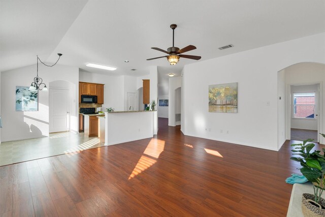 unfurnished living room featuring ceiling fan with notable chandelier, vaulted ceiling, plenty of natural light, and dark wood-type flooring