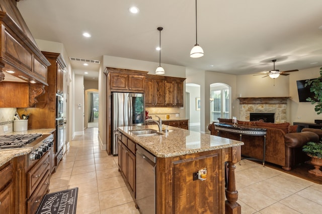 kitchen featuring sink, an island with sink, pendant lighting, a fireplace, and appliances with stainless steel finishes