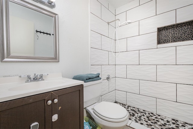 bathroom featuring a tile shower, vanity, and toilet