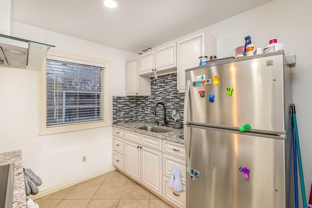 kitchen with stainless steel refrigerator, light stone countertops, sink, backsplash, and light tile patterned floors