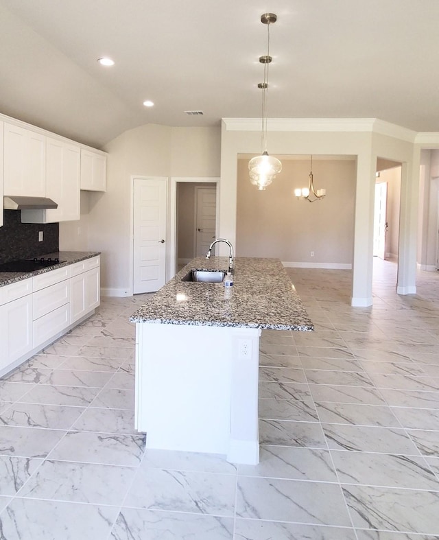 kitchen with a center island with sink, dark stone counters, decorative light fixtures, sink, and white cabinetry