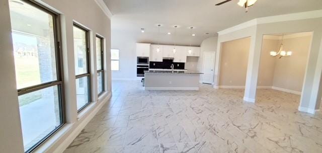 unfurnished living room with ceiling fan with notable chandelier and crown molding