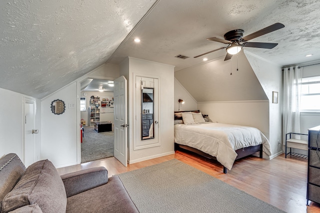 bedroom with ceiling fan, lofted ceiling, light wood-type flooring, and a textured ceiling