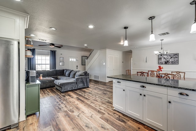 kitchen featuring hardwood / wood-style floors, white cabinets, ceiling fan with notable chandelier, stainless steel fridge, and decorative light fixtures