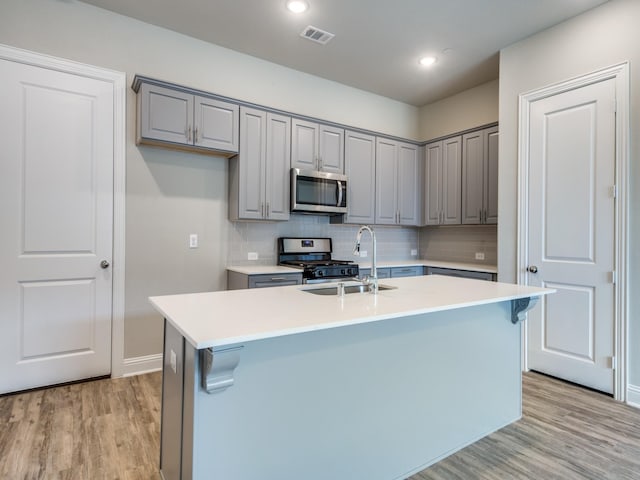 kitchen featuring light hardwood / wood-style floors, a kitchen island with sink, sink, and appliances with stainless steel finishes