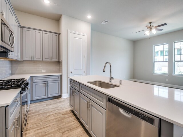 kitchen featuring gray cabinetry, sink, decorative backsplash, light wood-type flooring, and stainless steel appliances