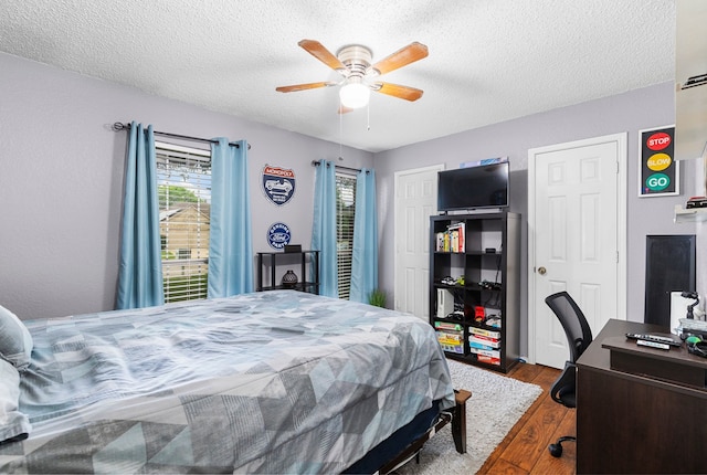 bedroom with two closets, ceiling fan, hardwood / wood-style floors, and a textured ceiling