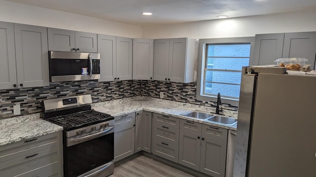 kitchen featuring gray cabinets, light stone counters, sink, and appliances with stainless steel finishes