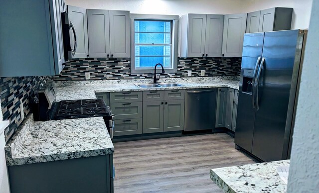 kitchen with sink, decorative backsplash, gray cabinets, light wood-type flooring, and stainless steel appliances