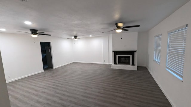 unfurnished living room with ceiling fan, dark hardwood / wood-style flooring, and a brick fireplace