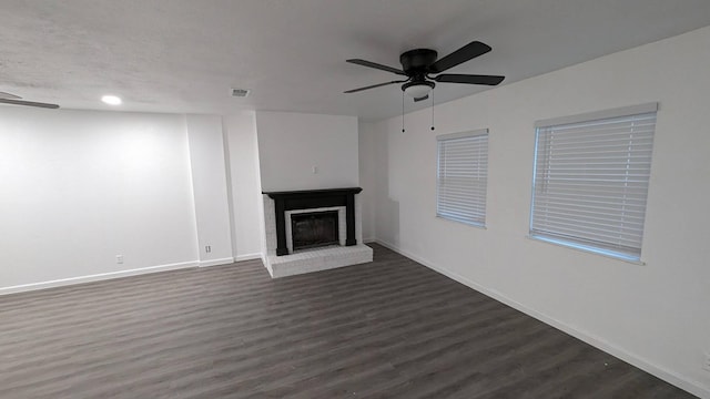 unfurnished living room with a brick fireplace, ceiling fan, and dark wood-type flooring