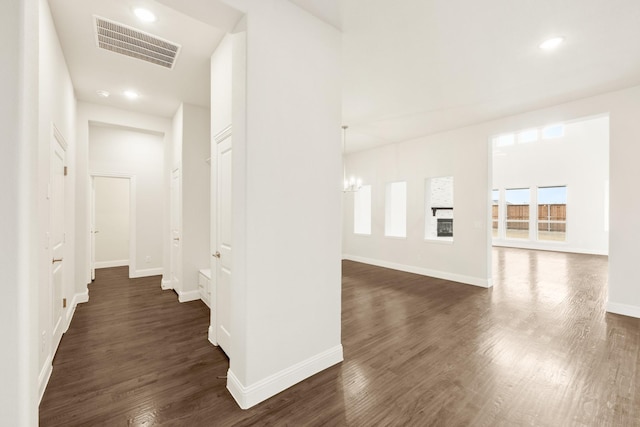 hall featuring a notable chandelier, baseboards, visible vents, and dark wood-style flooring