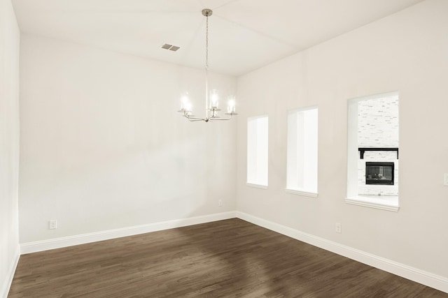 empty room featuring visible vents, baseboards, dark wood finished floors, a fireplace, and a notable chandelier