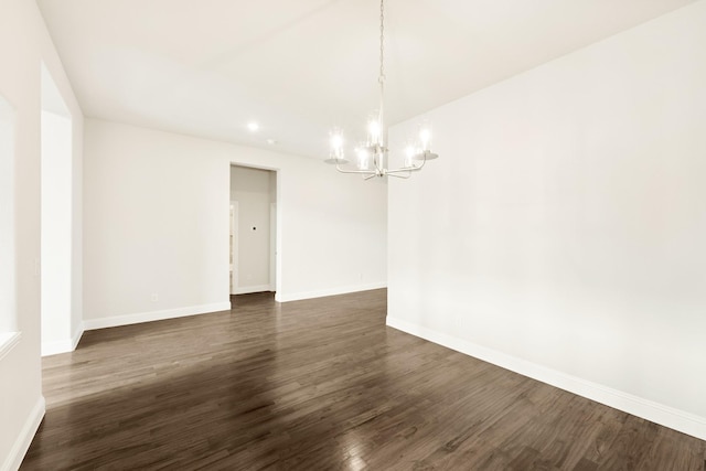 spare room with dark wood-style flooring, a notable chandelier, and baseboards