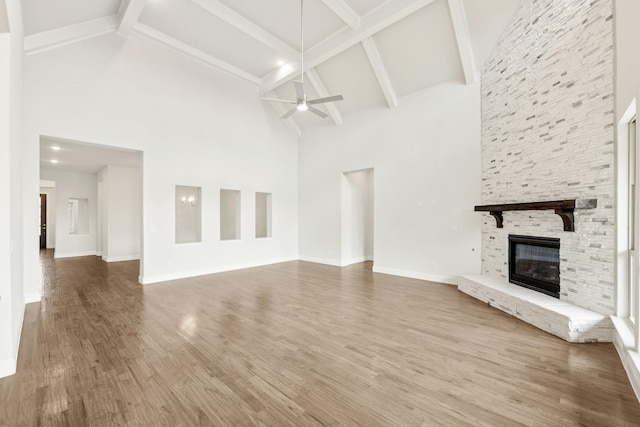 unfurnished living room featuring baseboards, ceiling fan, beamed ceiling, wood finished floors, and a stone fireplace