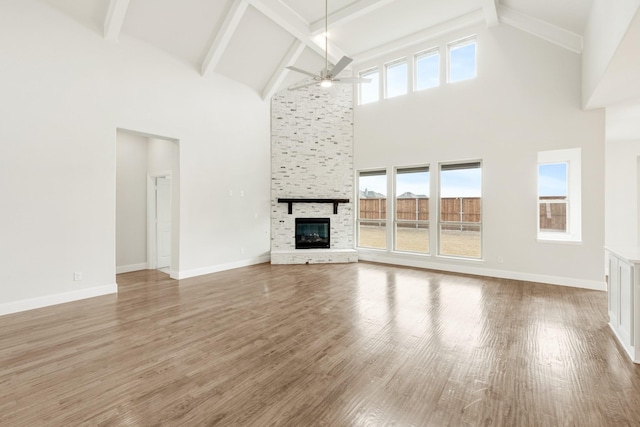 unfurnished living room with a large fireplace, ceiling fan, wood finished floors, and baseboards