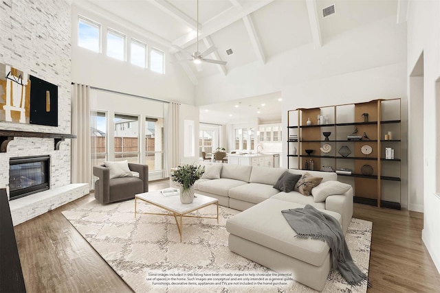 living room with a stone fireplace, plenty of natural light, wood finished floors, and visible vents