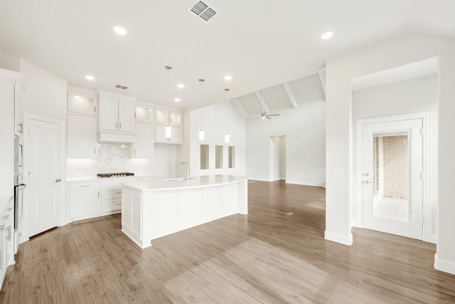 kitchen featuring light countertops, a center island with sink, glass insert cabinets, and white cabinets