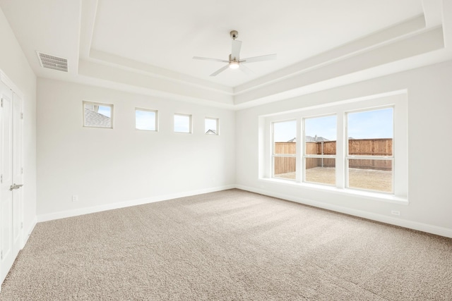 carpeted empty room featuring ceiling fan, a tray ceiling, visible vents, and baseboards