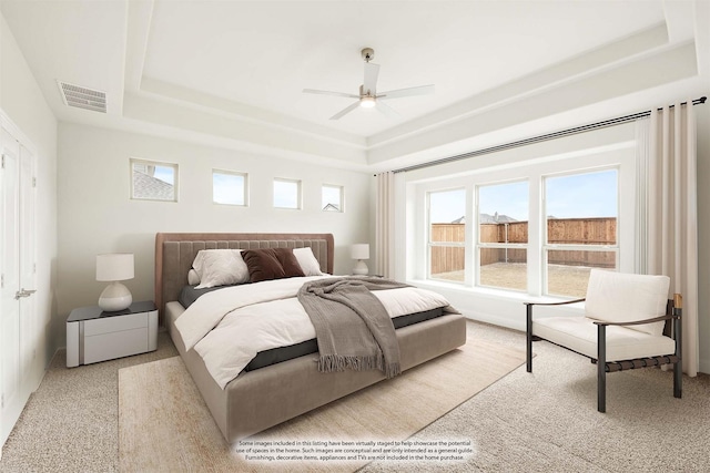 bedroom with light carpet, visible vents, a raised ceiling, and a ceiling fan