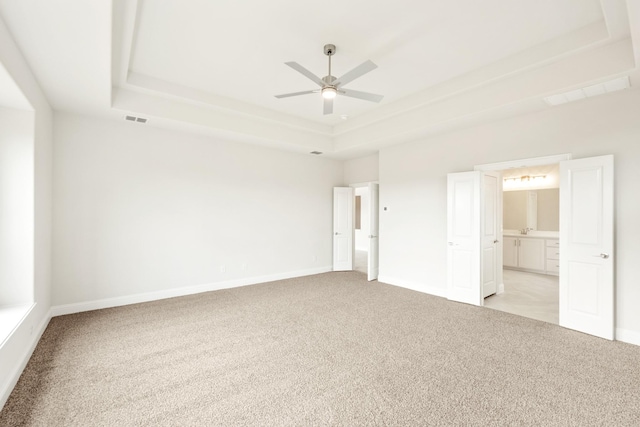 unfurnished bedroom with connected bathroom, light colored carpet, visible vents, baseboards, and a raised ceiling